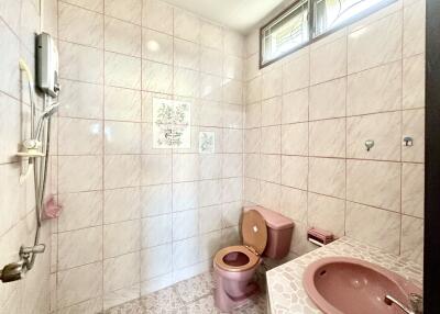 A bathroom with tiled walls, a pink toilet, a pink sink, and a shower area.