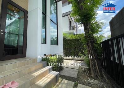 Exterior view of the house showing the entrance with stairs, garden area, and neighboring properties