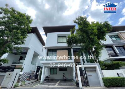 Front view of a modern residential building with multiple floors, trees, and driveway.