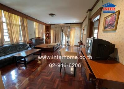 Spacious living room with wooden floor, a sofa set, TV, and table, well lit with natural light from large windows