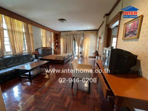 Spacious living room with wooden floor, a sofa set, TV, and table, well lit with natural light from large windows