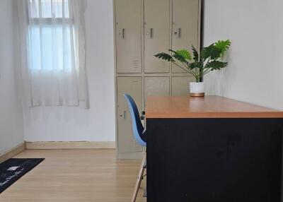 Room with lockers, desk, chair, potted plant, single window with white curtains