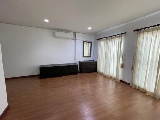 Spacious living room with wooden flooring, large windows with curtains, and air conditioning.