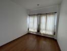 Empty bedroom with hardwood floor and curtained windows