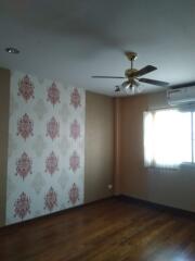 Bedroom with wooden flooring, a ceiling fan, a wallpapered accent wall, air conditioning unit, and a window with curtains