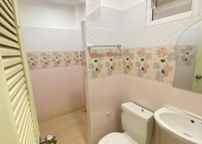 Compact bathroom with floral tiled wall, toilet, sink, and standing shower