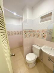 Compact bathroom with floral tiled wall, toilet, sink, and standing shower