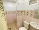 Compact bathroom with floral tiled wall, toilet, sink, and standing shower