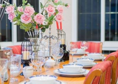 A dining room with a neatly set table, adorned with pink flowers and elegant crockery.