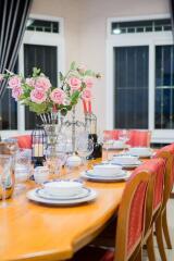 A dining room with a neatly set table, adorned with pink flowers and elegant crockery.