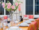 A dining room with a neatly set table, adorned with pink flowers and elegant crockery.