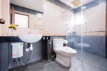 Modern bathroom with glass shower door, toilet, sink, and water heater