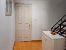 Hallway with wooden floor and white walls leading to a door