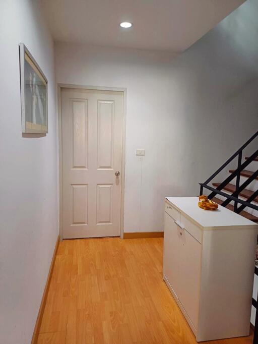 Hallway with wooden floor and white walls leading to a door