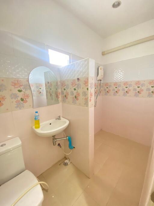 Small bathroom with floral wall tiles, sink, toilet, and water heater