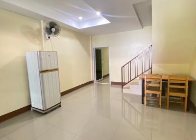 Spacious open living area with white tiled flooring, ceiling fan, staircase, and refrigerator