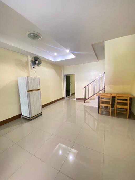 Spacious open living area with white tiled flooring, ceiling fan, staircase, and refrigerator