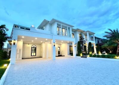 Front view of a modern, two-story house with large windows, a spacious driveway, and exterior lighting