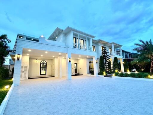 Front view of a modern, two-story house with large windows, a spacious driveway, and exterior lighting