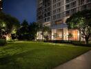 Modern apartment building with well-lit green lawn at night