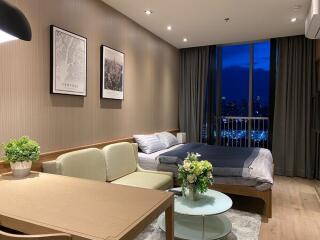 Living room with a dining area, sofa, and bed in an apartment with a city view