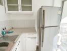 Compact modern kitchen with white cabinetry and stainless steel refrigerator