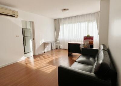 Spacious living room with black leather sofa, window with curtains, and wooden floor