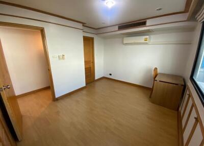 A spacious bedroom with wooden flooring, a small desk, air conditioning, and a window.