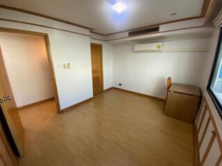 A spacious bedroom with wooden flooring, a small desk, air conditioning, and a window.