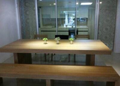 Modern dining area with wooden table and benches, adjacent to glass-partitioned kitchen