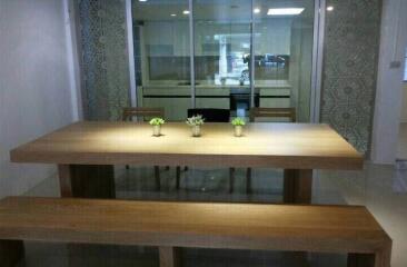 Modern dining area with wooden table and benches, adjacent to glass-partitioned kitchen