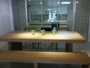 Modern dining area with wooden table and benches, adjacent to glass-partitioned kitchen