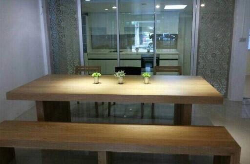 Modern dining area with wooden table and benches, adjacent to glass-partitioned kitchen