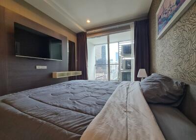 Modern bedroom with large bed, wall-mounted TV, and a balcony with city view