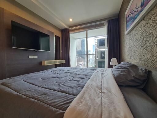 Modern bedroom with large bed, wall-mounted TV, and a balcony with city view