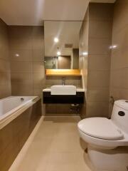 Modern bathroom with beige tiles, a bathtub, a washbasin, and a toilet