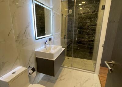 Modern bathroom with illuminated mirror, vanity sink, toilet, and glass-enclosed shower