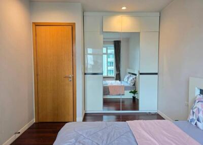 Modern bedroom with wooden door, built-in mirrored wardrobe, and neatly made bed with patterned pillows and blankets.