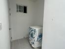 Small laundry area with a washing machine, tiled floor, and a small window.