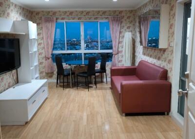 Well-lit living room with wooden floors, a red sofa, and a dining area with a city view