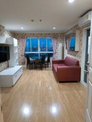 Well-lit living room with wooden floors, a red sofa, and a dining area with a city view