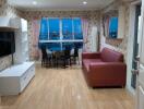 Well-lit living room with wooden floors, a red sofa, and a dining area with a city view