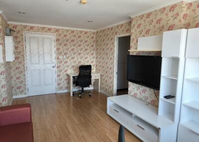 A living room with a TV, desk, and chair, featuring floral wallpaper