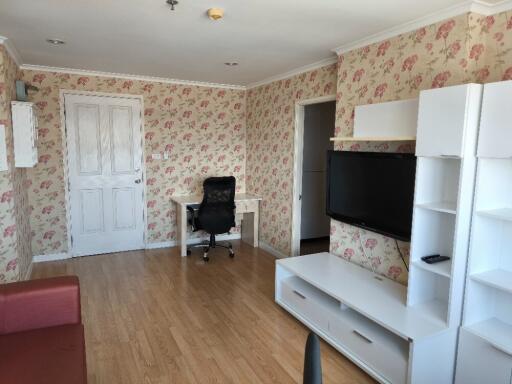 A living room with a TV, desk, and chair, featuring floral wallpaper