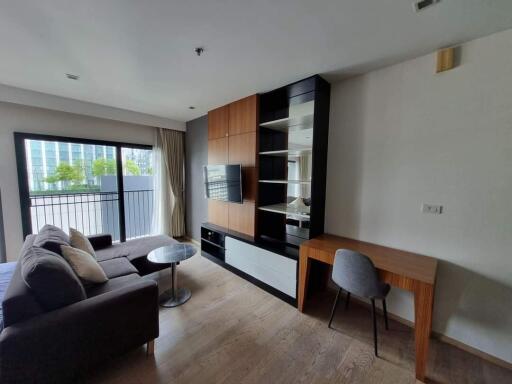 Modern living room with a couch, built-in TV unit, desk, and large balcony door