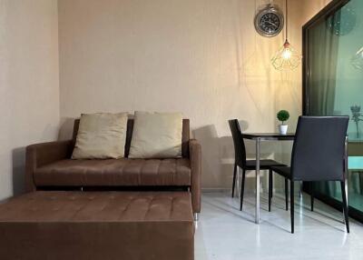 Modern living room with a brown sofa, glass dining table, and wall clock