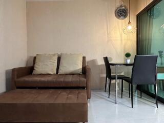 Modern living room with a brown sofa, glass dining table, and wall clock