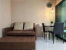 Modern living room with a brown sofa, glass dining table, and wall clock