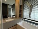 Modern bathroom with a large mirror, sink, bathtub, and window with blinds