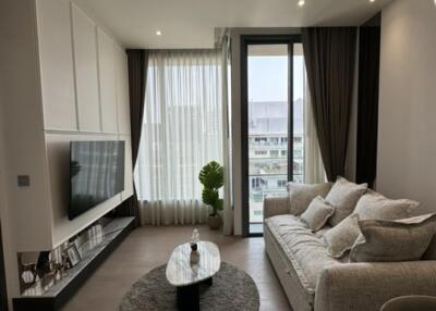 Modern living room with a large sofa, mounted TV, and large window with sheer curtains